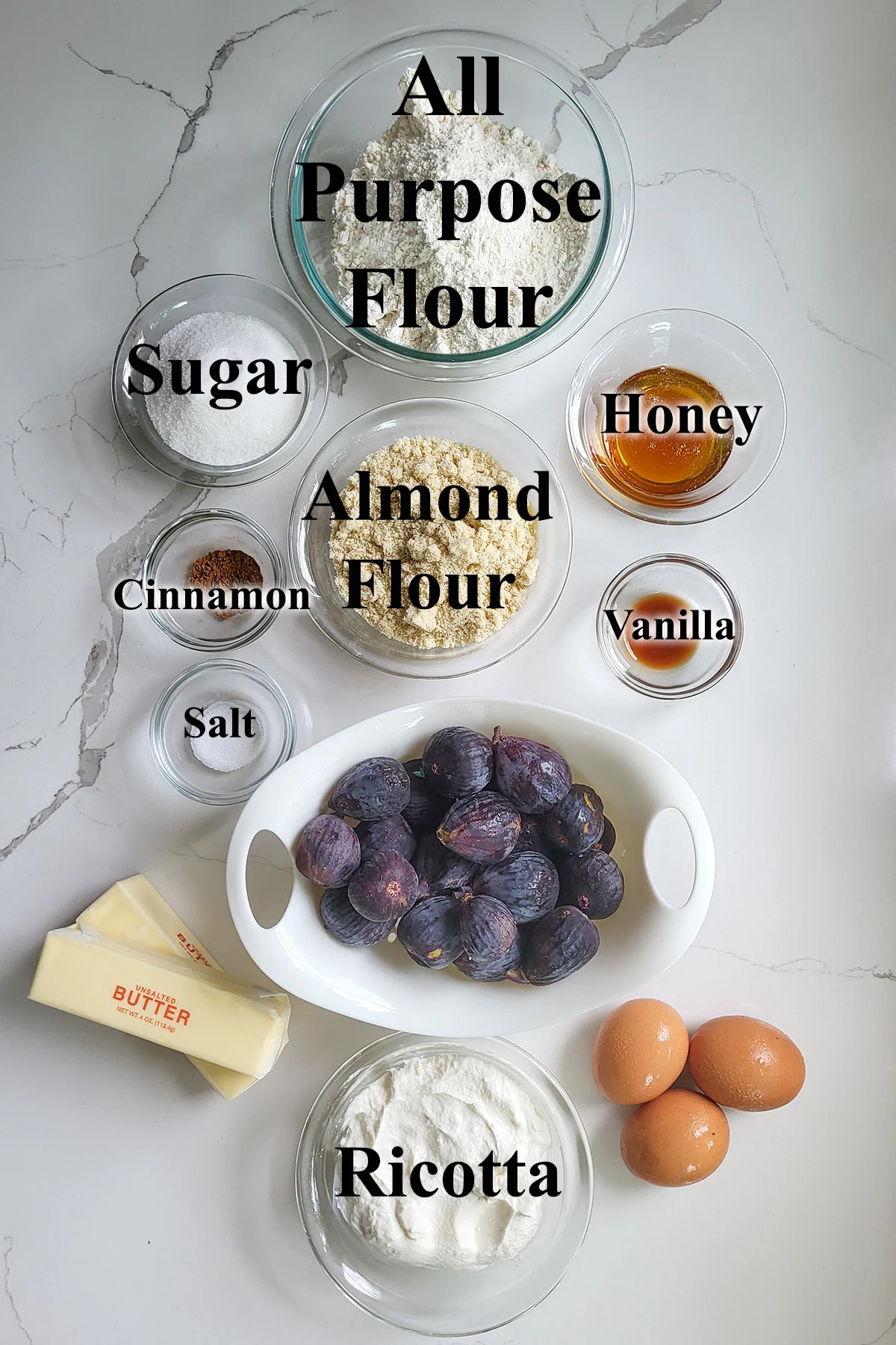 ingredients for fig tart in glass bowls on a white surface.