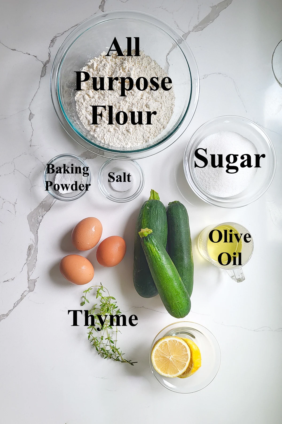 ingredients for lemon zucchini bread in glass bowls on a white surface. 