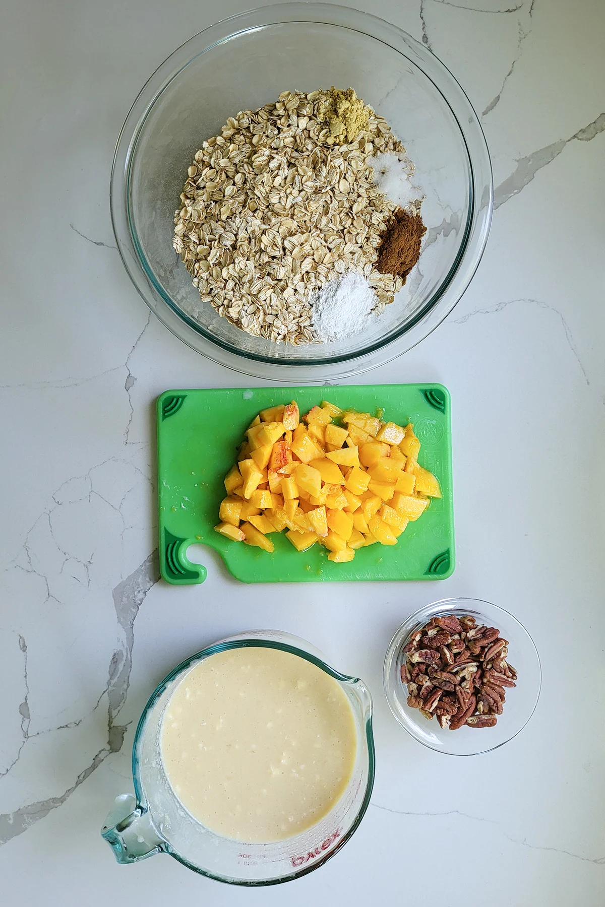 a bowl of oats and spices, a chopped peach, a bowl of pecan pieces and a cup of milk.