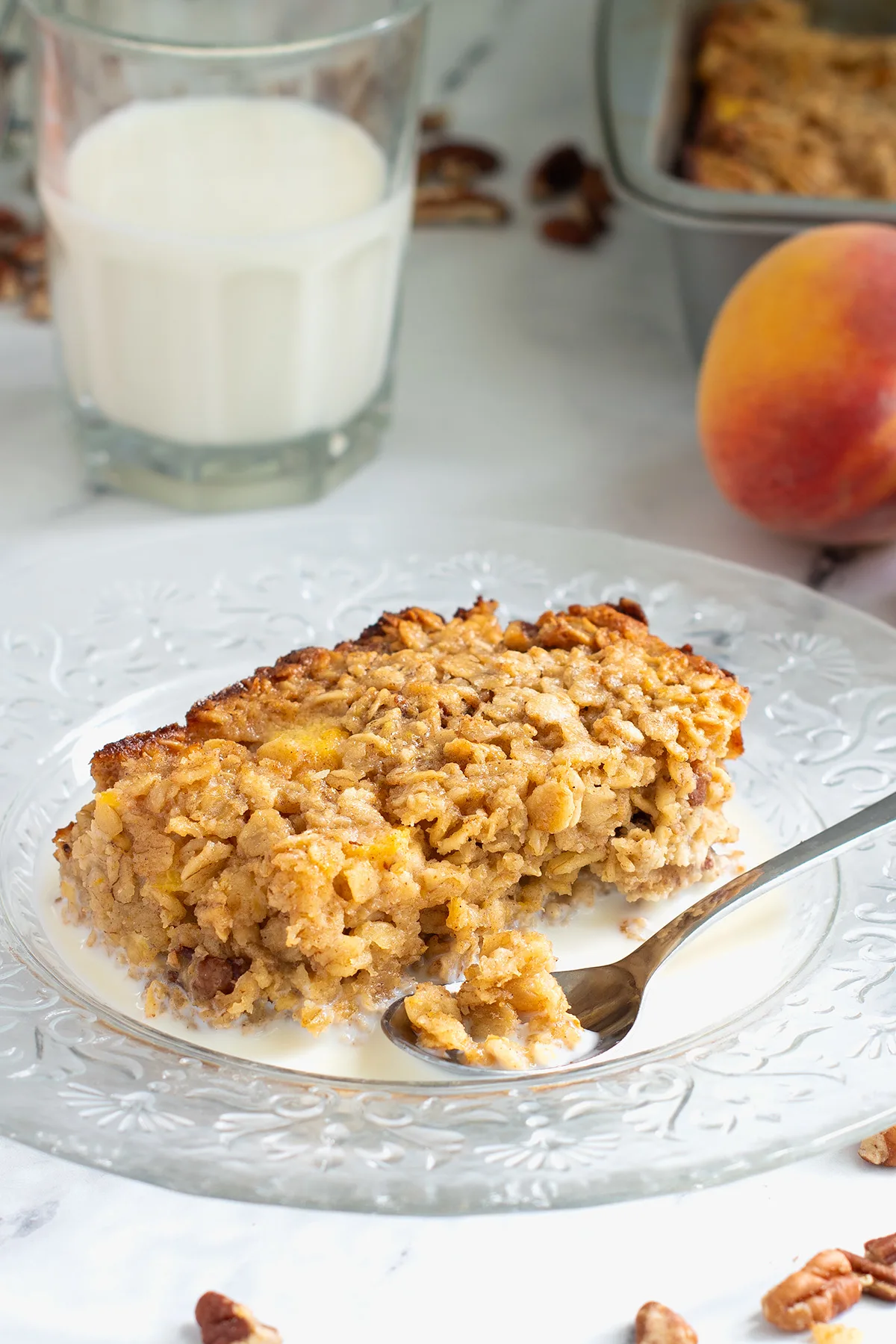 a slice of peach baked oatmeal on a plate with milk and a spoon.
