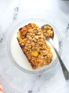 a slice of peach baked oatmeal on a glass plate with milk and a spoon.