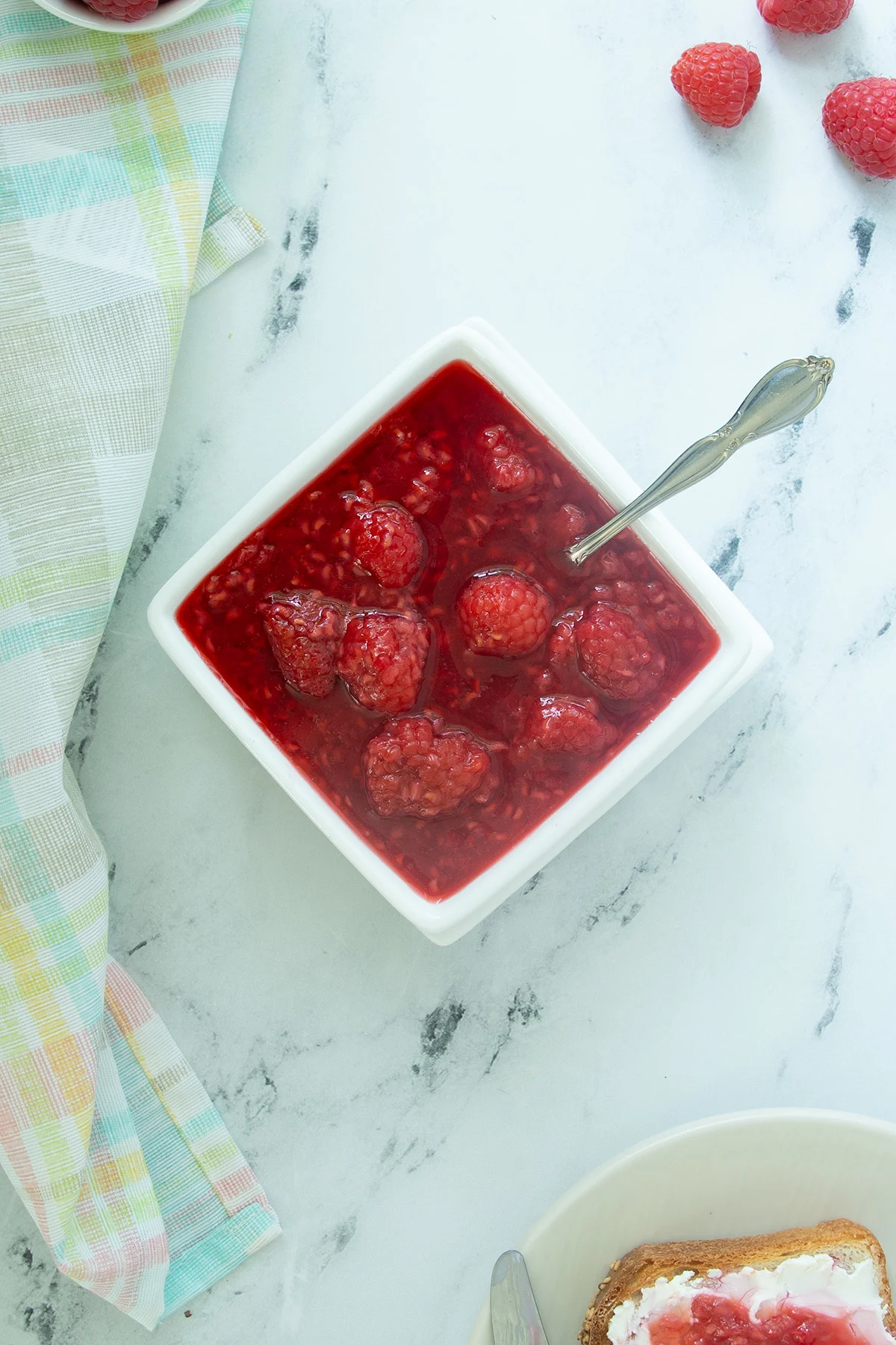 a white bowl with raspberry compote on a white surface.