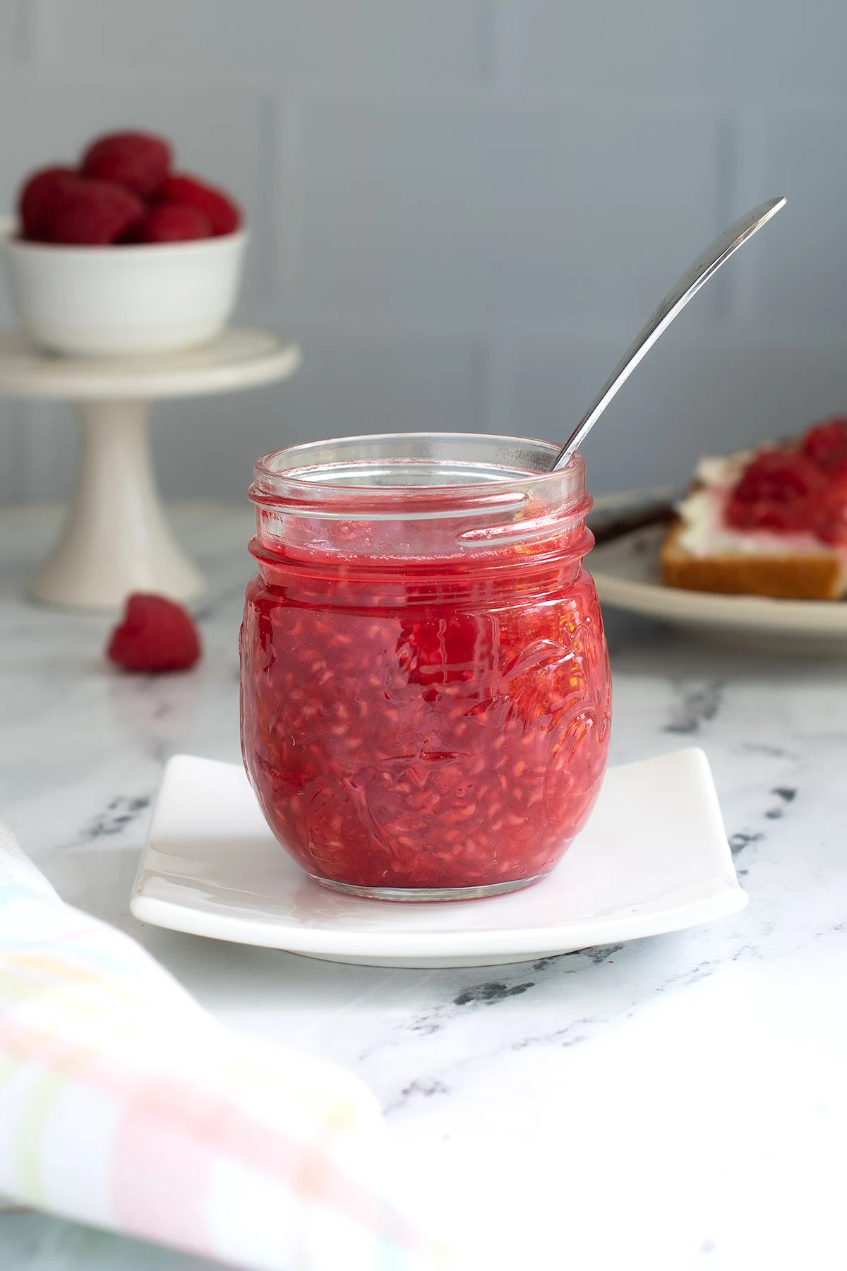 a jar full of raspberry compote with a spoon in it.