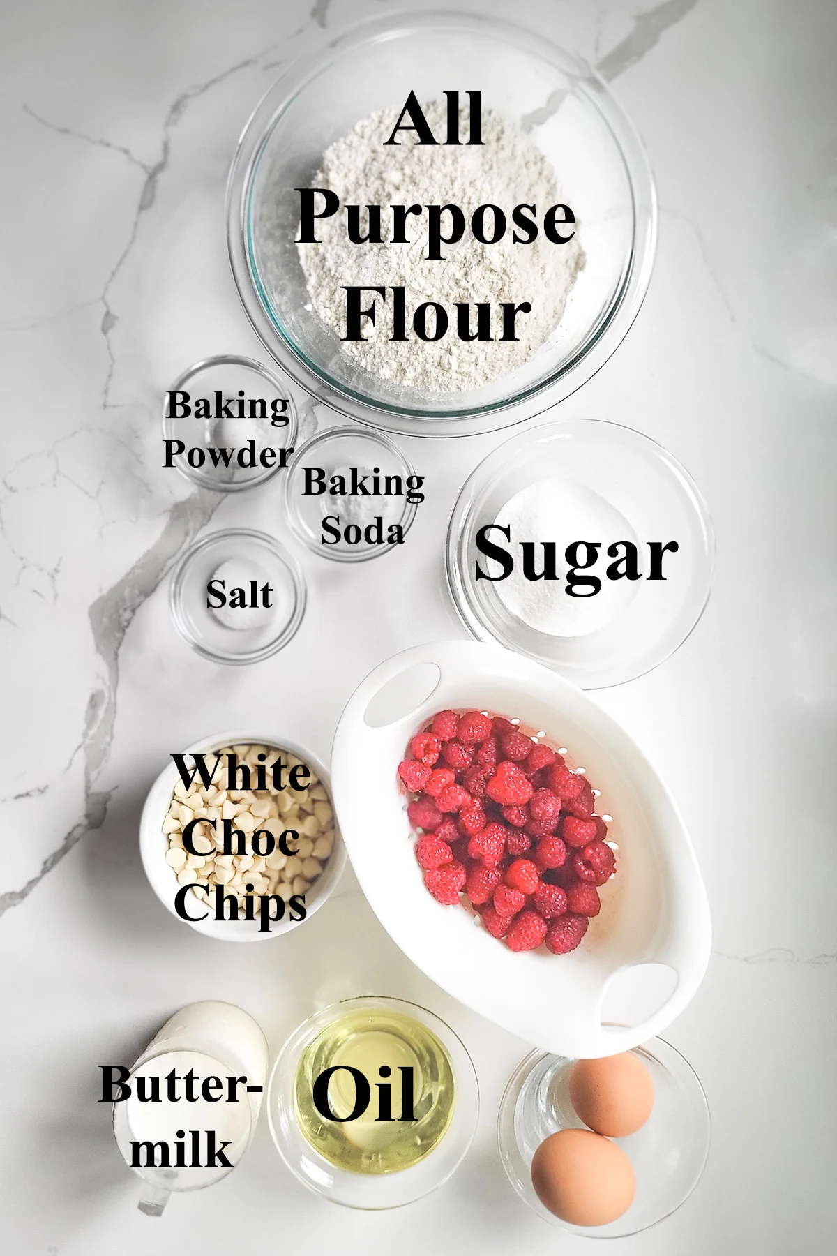 ingredients for making raspberry muffins in glass bowls on a white surface.
