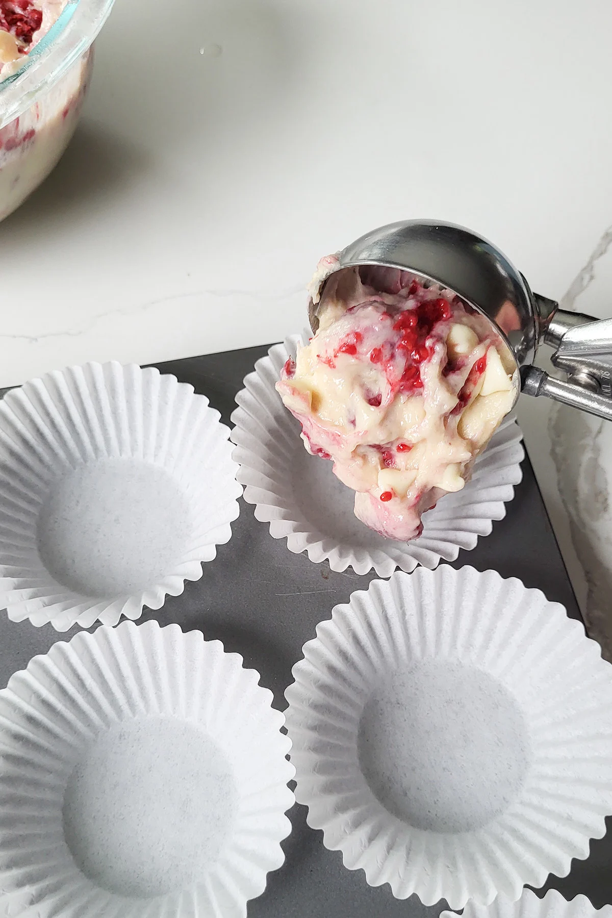 a scooper putting raspberry muffin batter into a paper lined muffin tin.