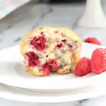 half of a raspberry muffin on a white plate.