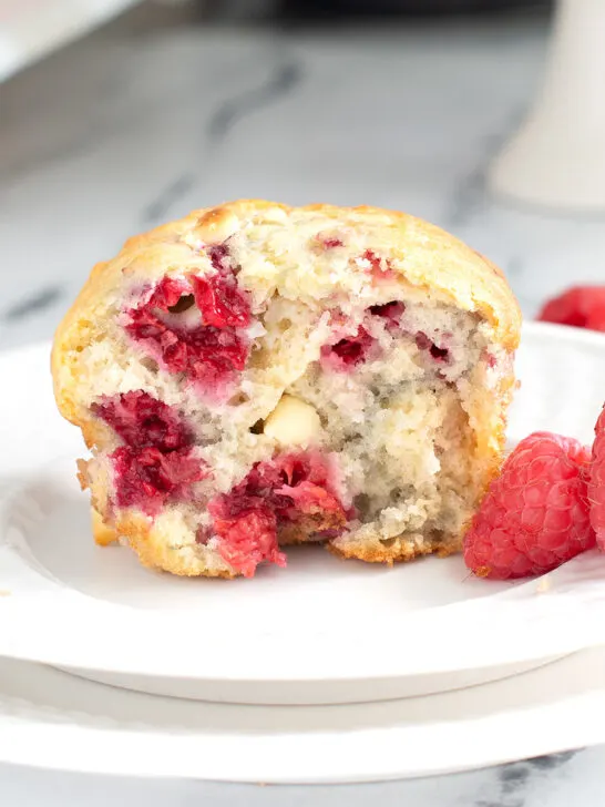 half of a raspberry muffin on a white plate.