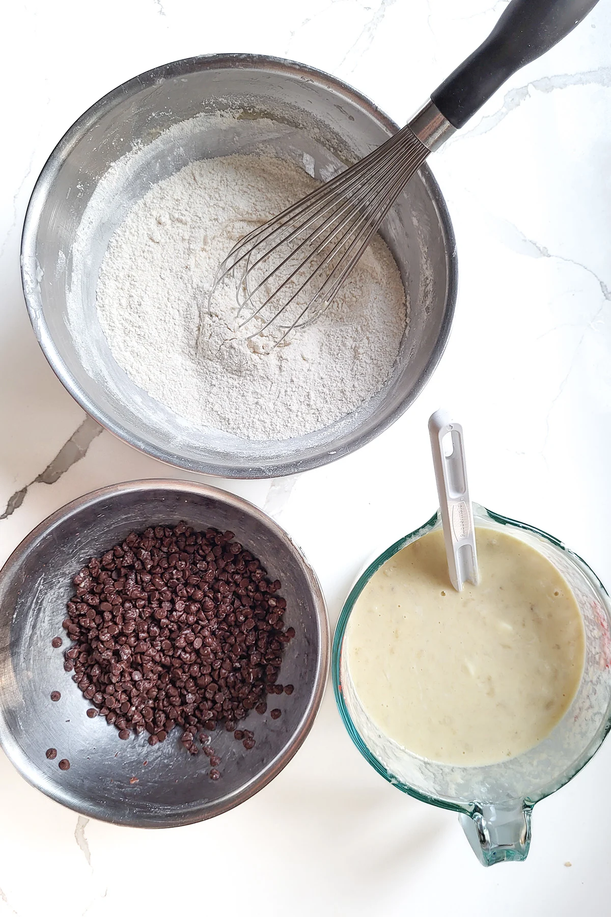 A bowl of dry ingredients, a bowl of wet ingredients and a bowl of chocolate chips.