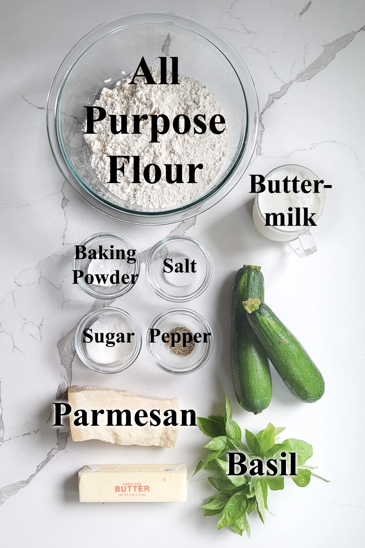 ingredients for making zucchini biscuits in glass bowls on a white surface.