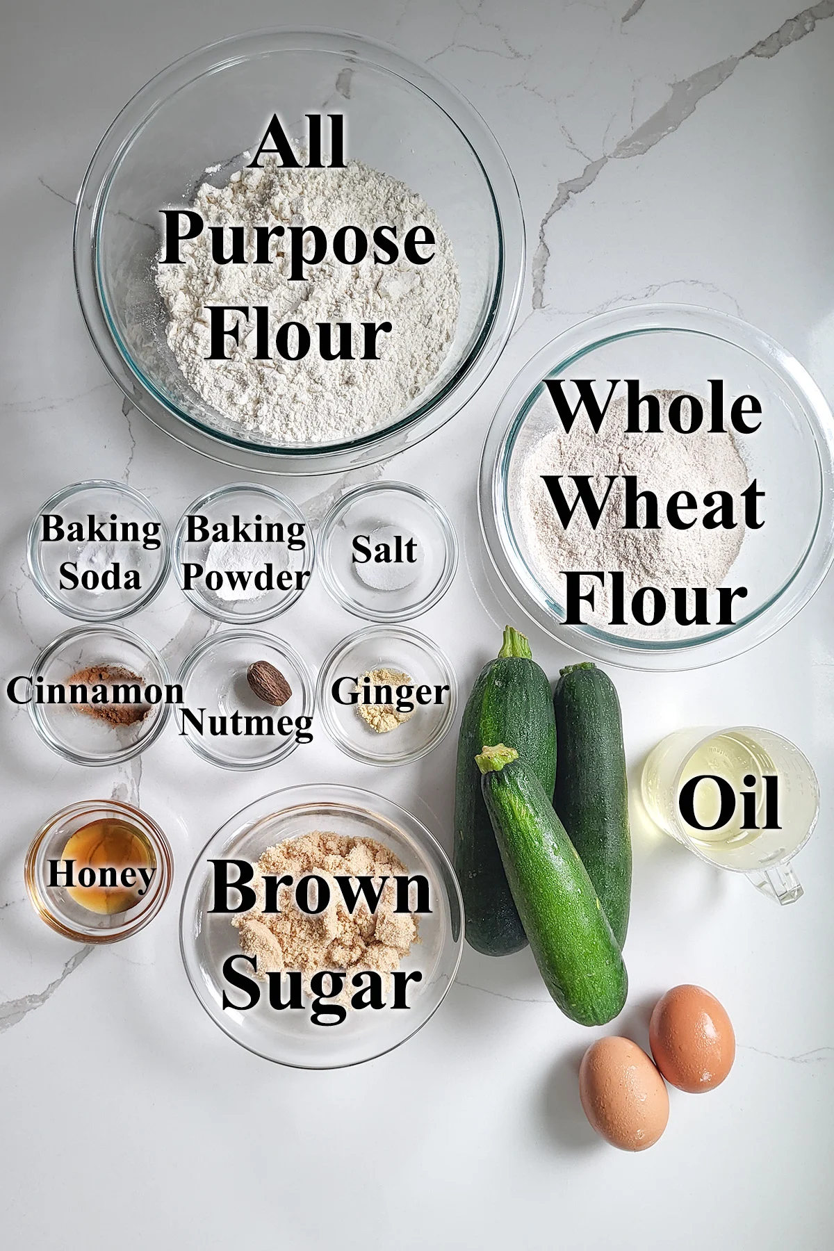 ingredients for whole wheat zucchini bread in glass bowls on a white surface.