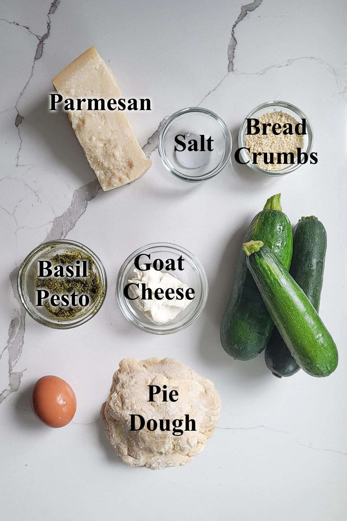 ingredients for zucchini galette in glass bowls on a white surface.