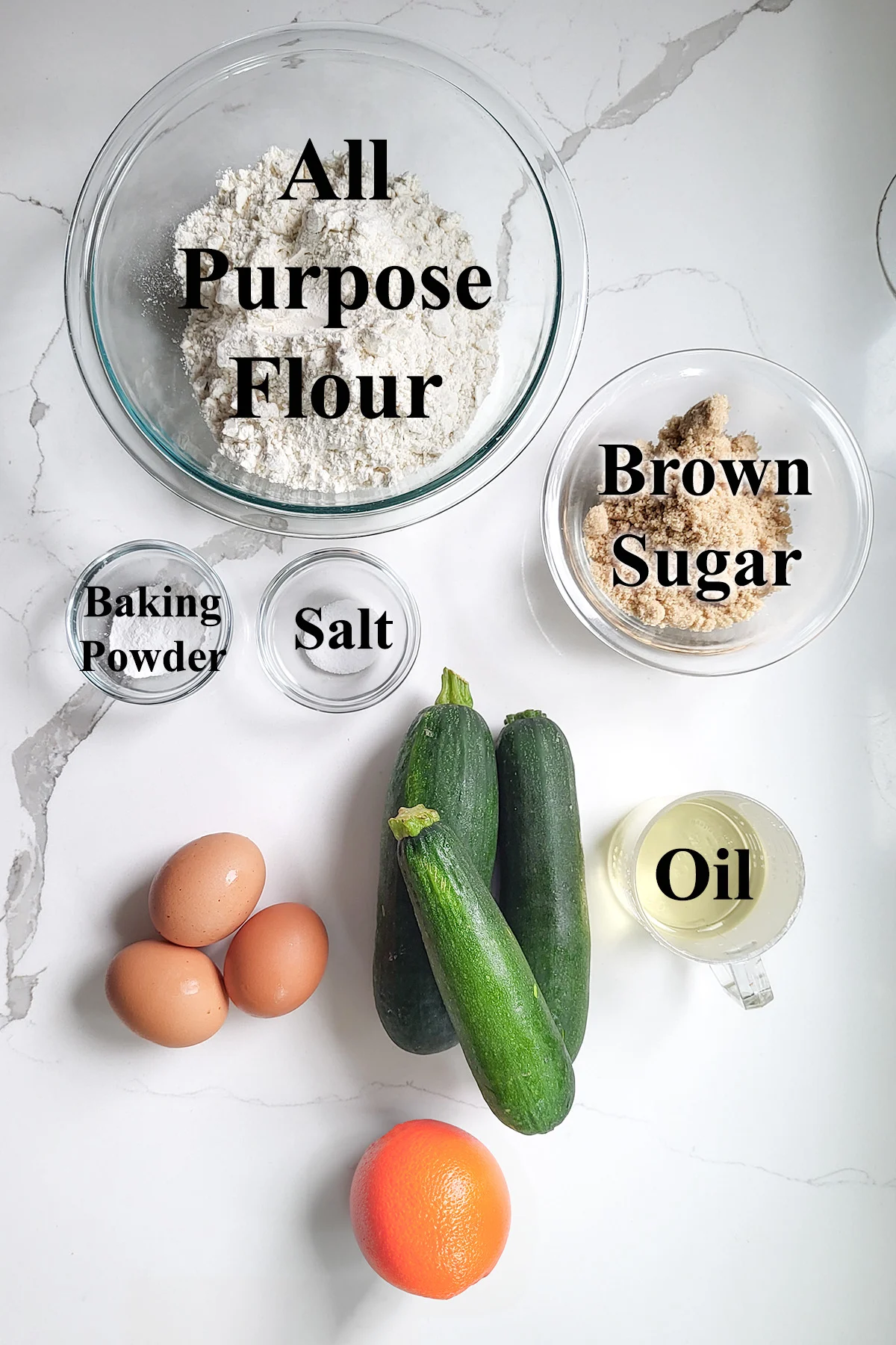 ingredients for zucchini muffins in glass bowls on a white surface.