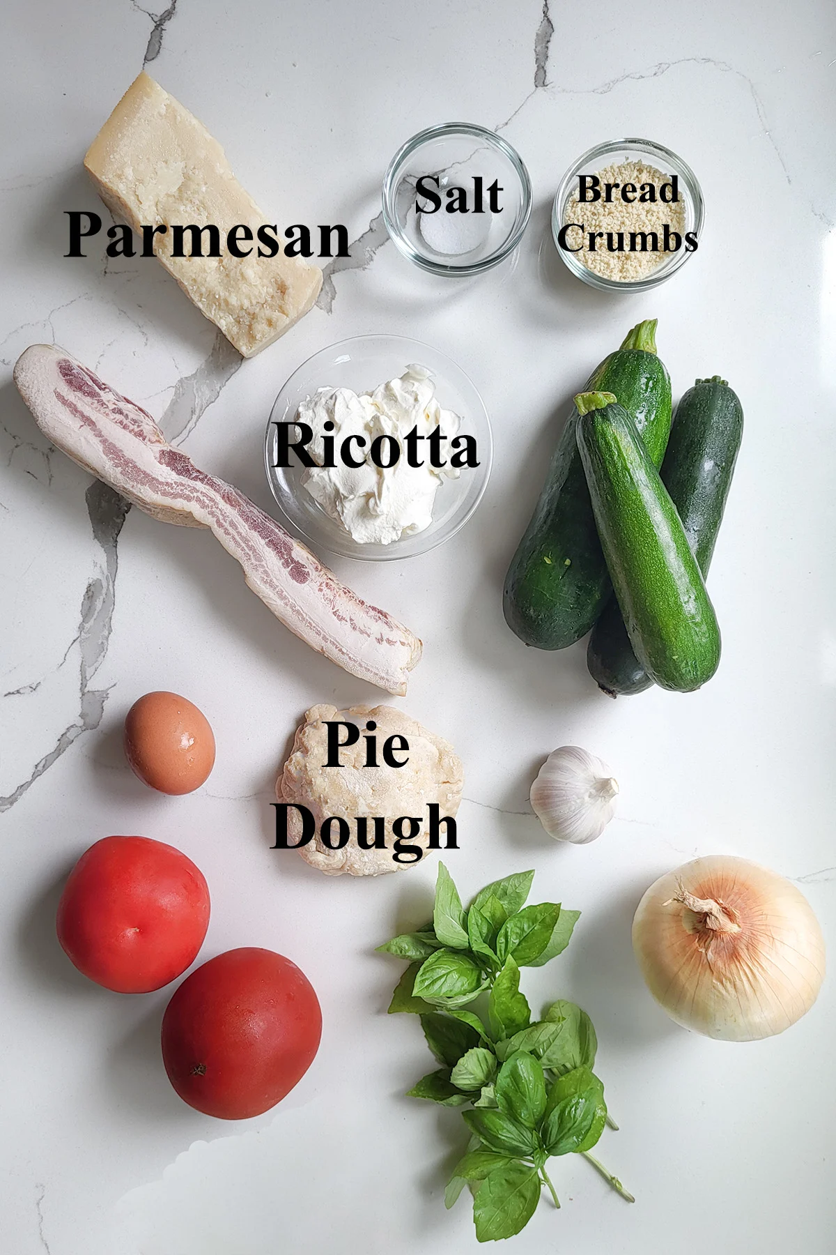 ingredients for zucchini and ricotta pie in glass bowls on a white surface.