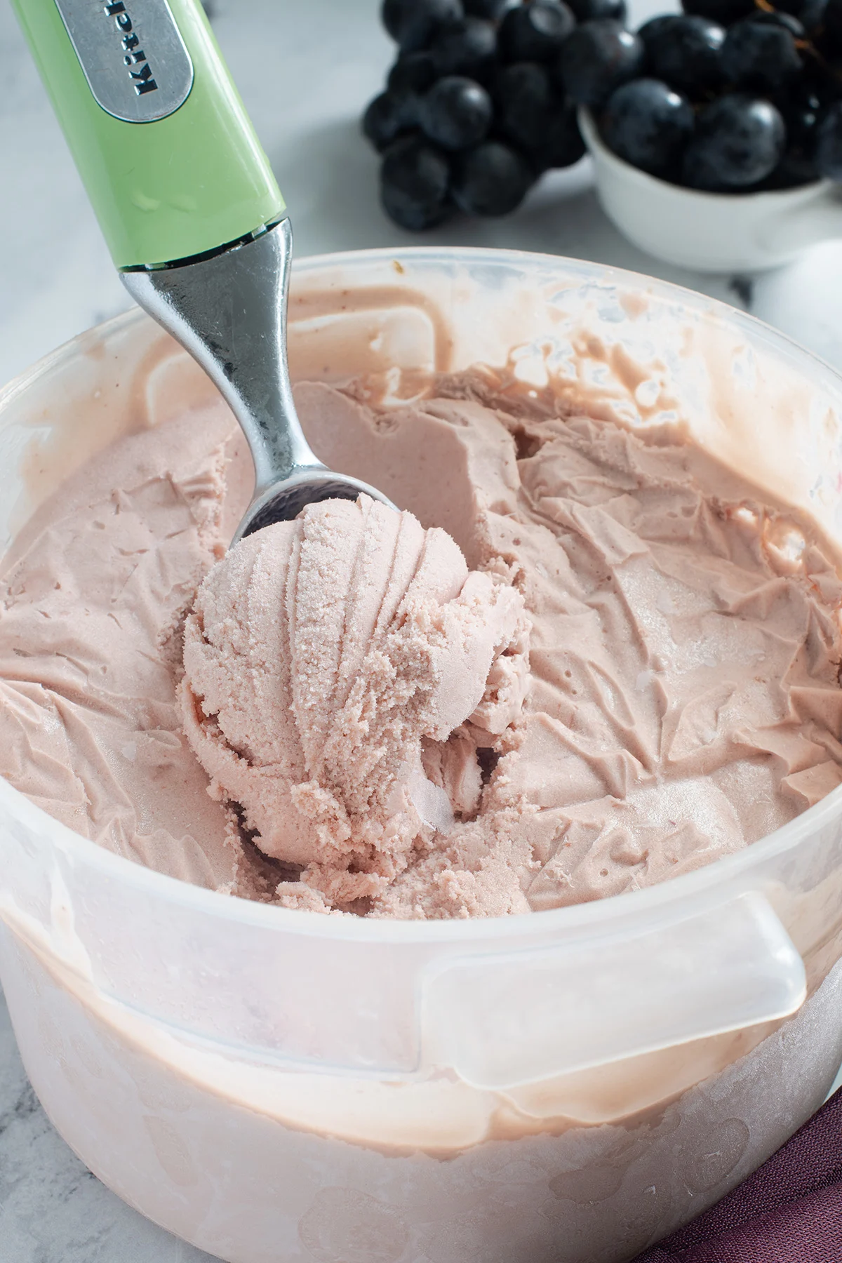 a container of concord grape ice cream with an ice cream scoop in it.