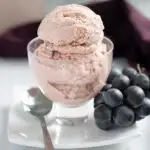 a glass dish with grape ice cream in a white plate with a cluster of grapes.