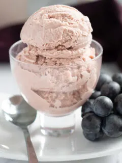 a glass dish with grape ice cream in a white plate with a cluster of grapes.