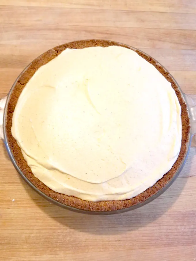 a pumpkin mousse pie with no topping on a wood surface.
