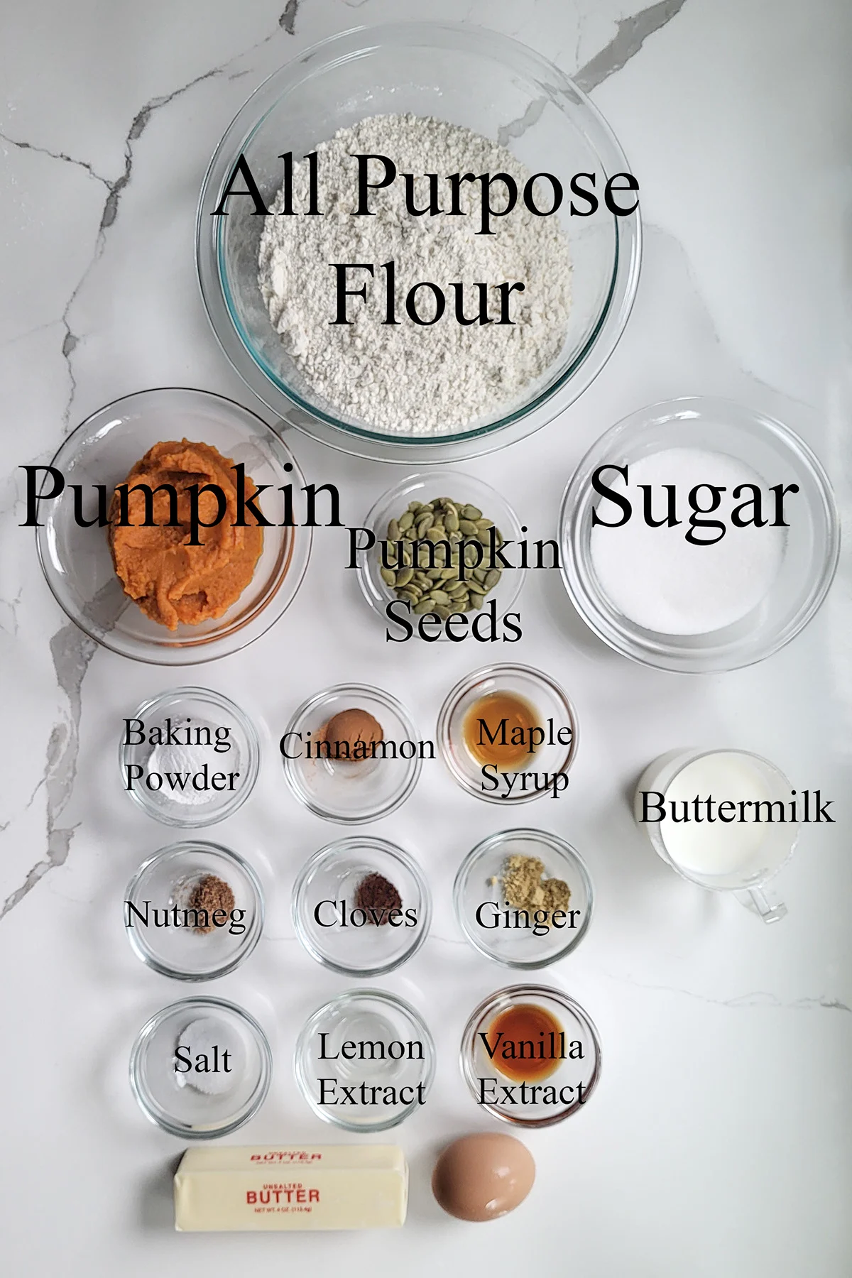 ingredients for pumpkin scones in glass bowls on a white surface. 