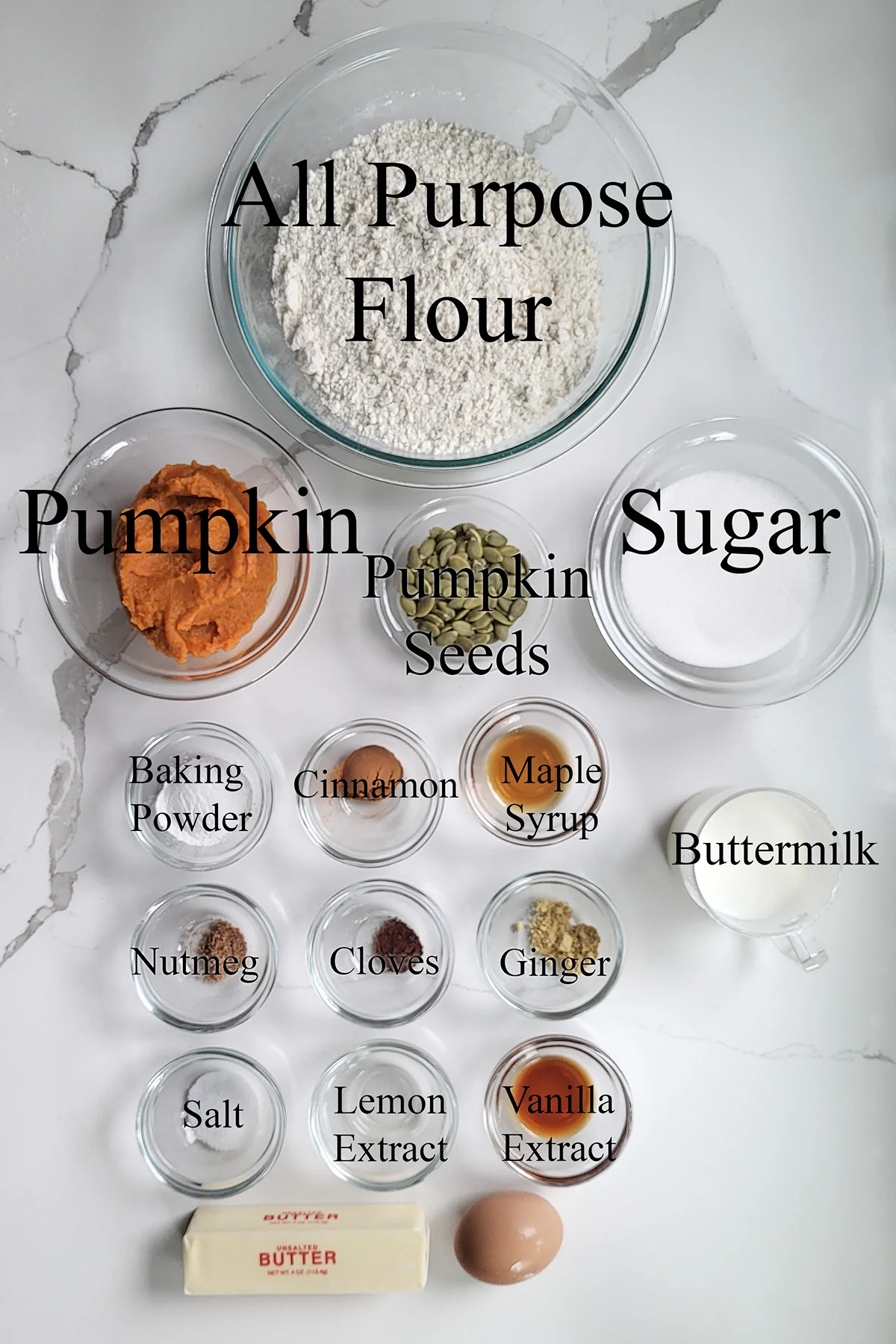 ingredients for pumpkin scones in glass bowls on a white surface.