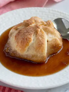 an apple dumpling with brown sugar syrup on a white plate.