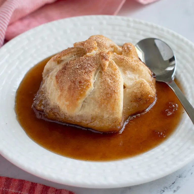 an apple dumpling with brown sugar syrup on a white plate.