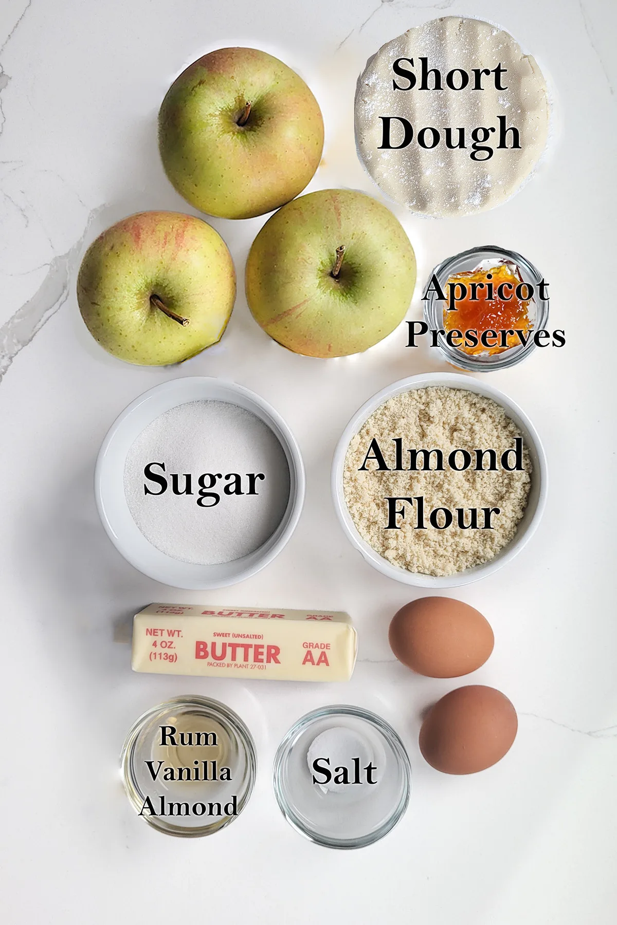 ingredients for apple frangipane tart in bowls on a white surface. 