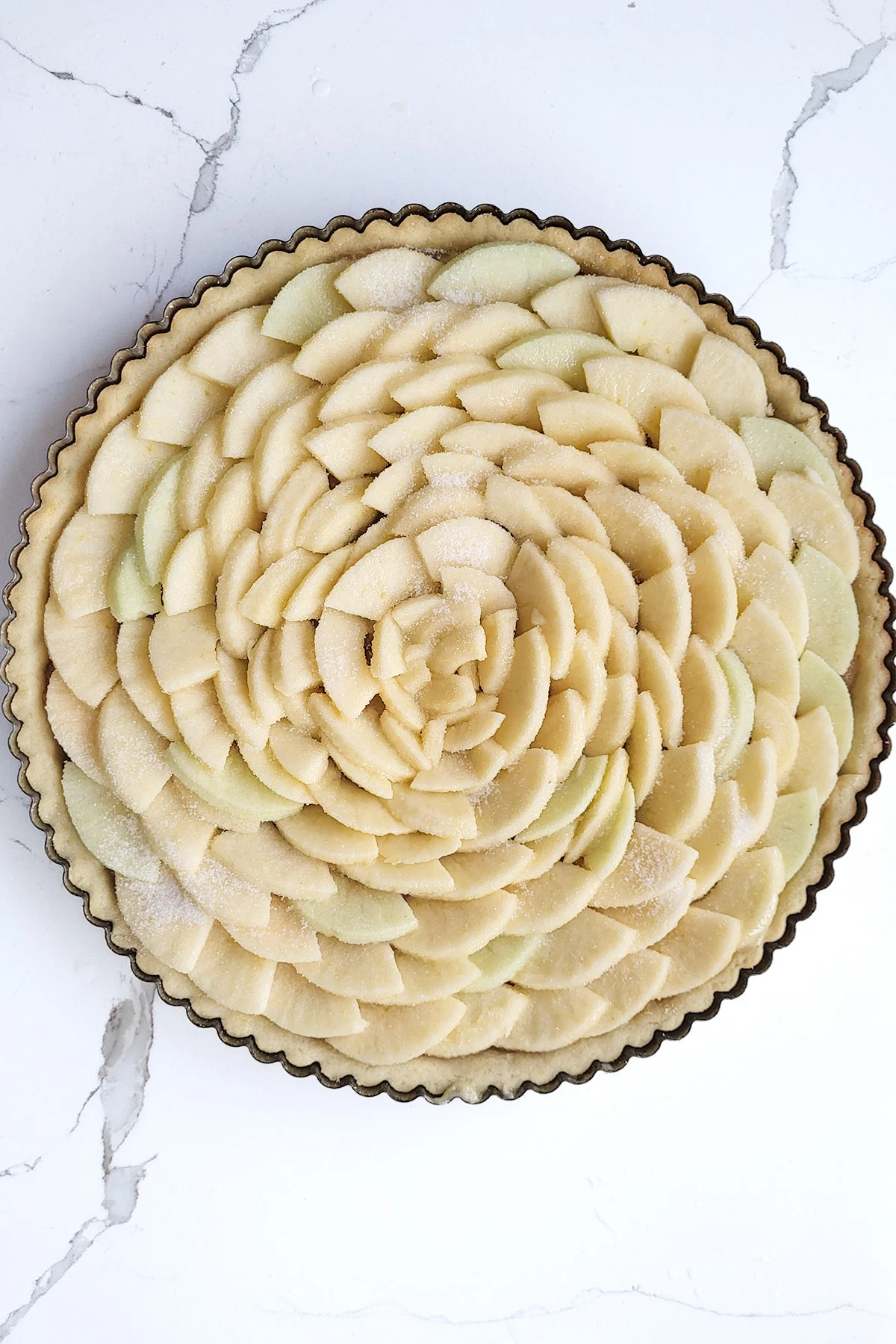 an unbaked apple tart on a white surface.
