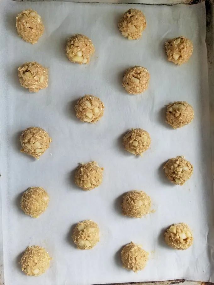 balls of apple oatmeal cookie dough on a parchment lined sheet pan.