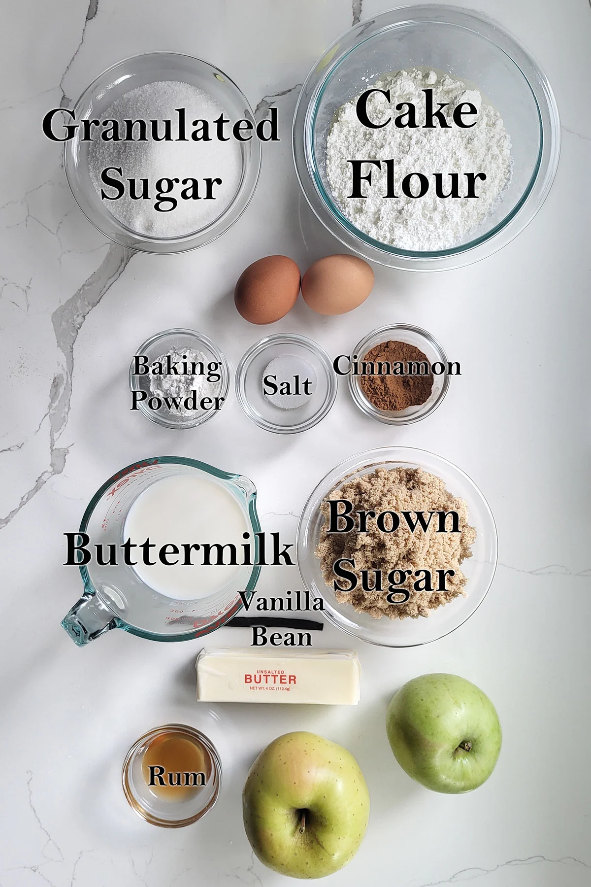 ingredients for apple upside down cake in glass bowls on a white surface.