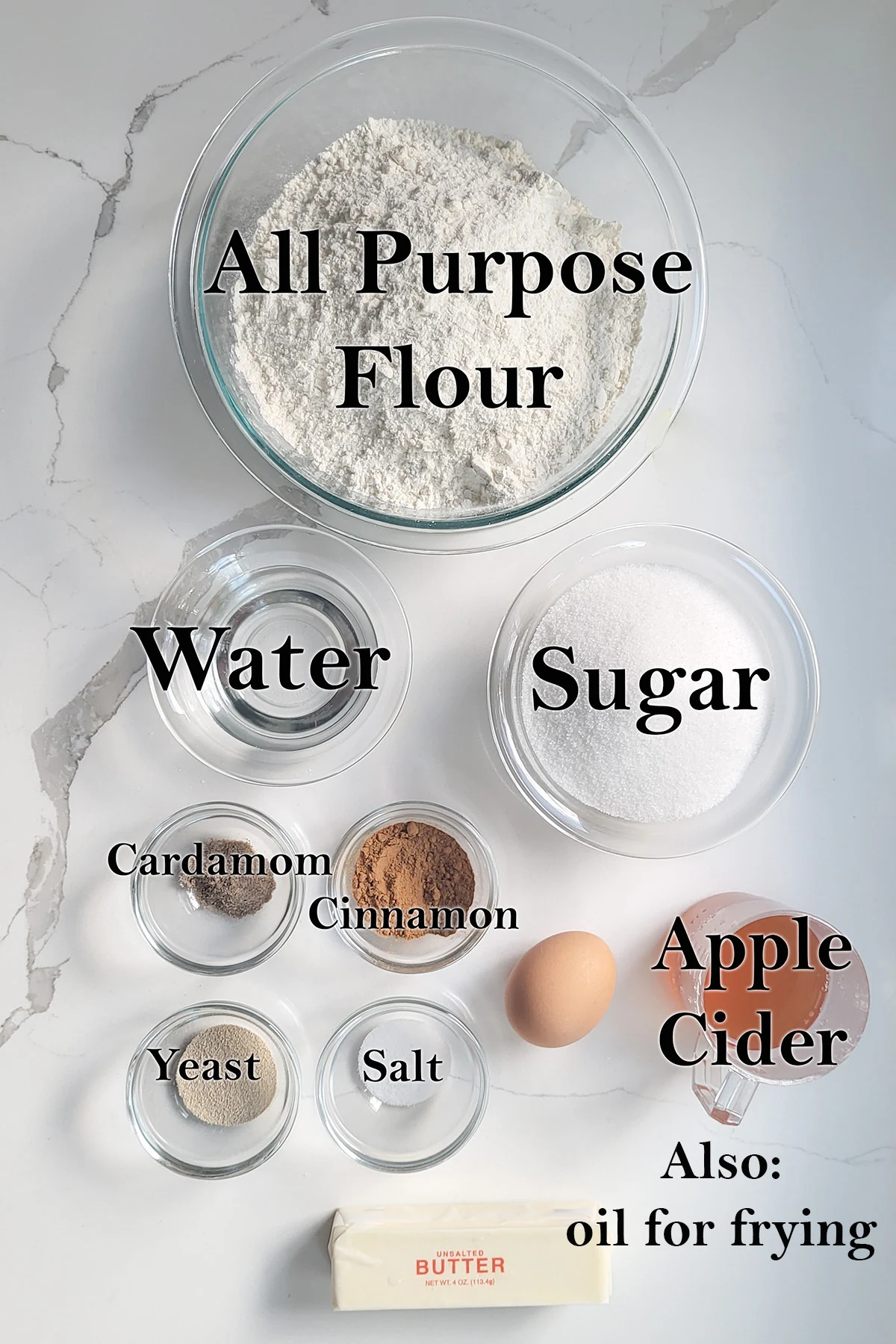 ingredients for cider donuts in glass bowls on a white surface.