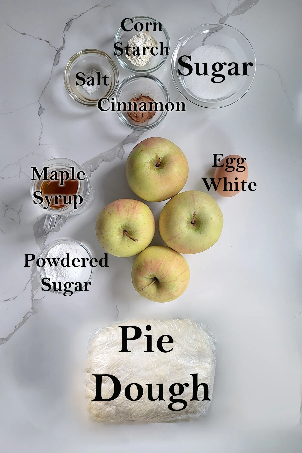 Ingredients for maple apple pie in glass bowls on a white surface.