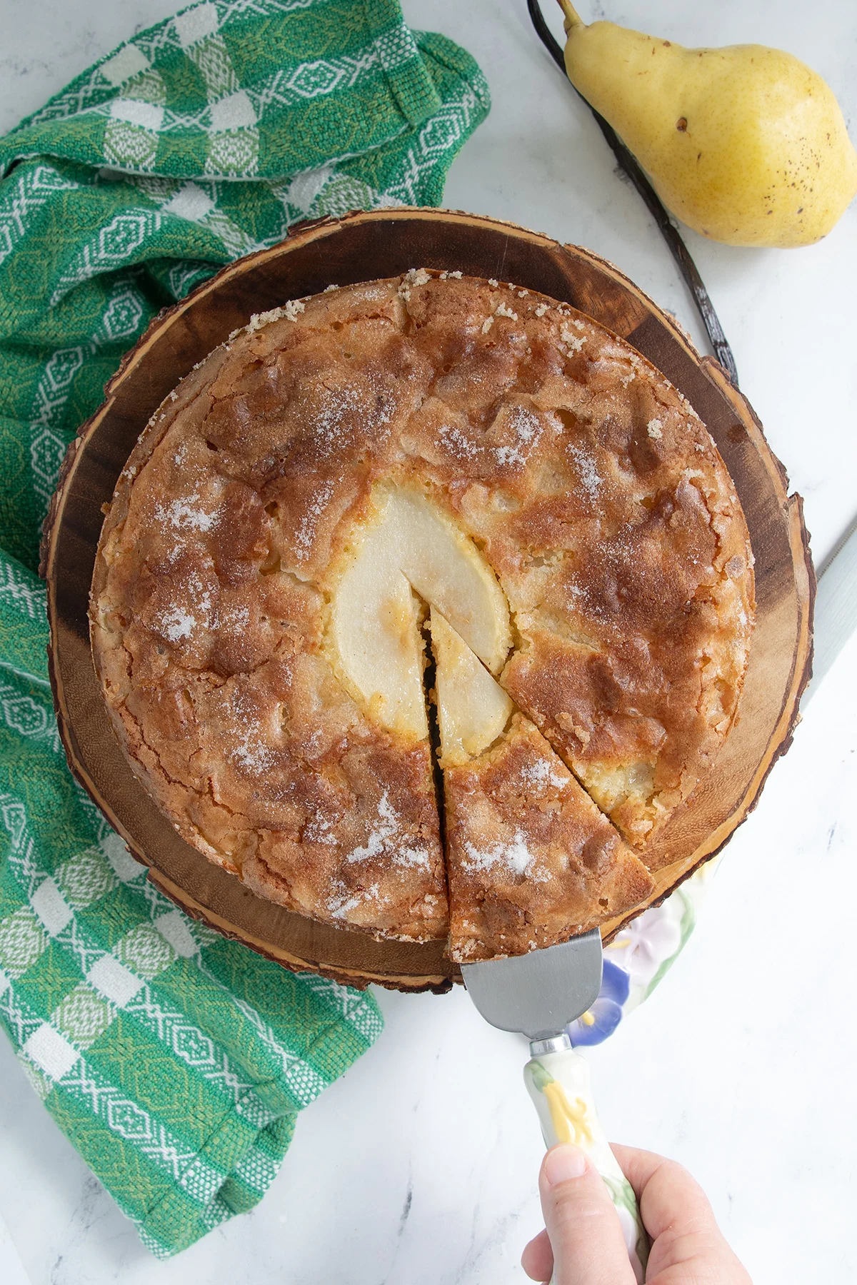 a pear cake on a wooden cake stand with a slice cut.