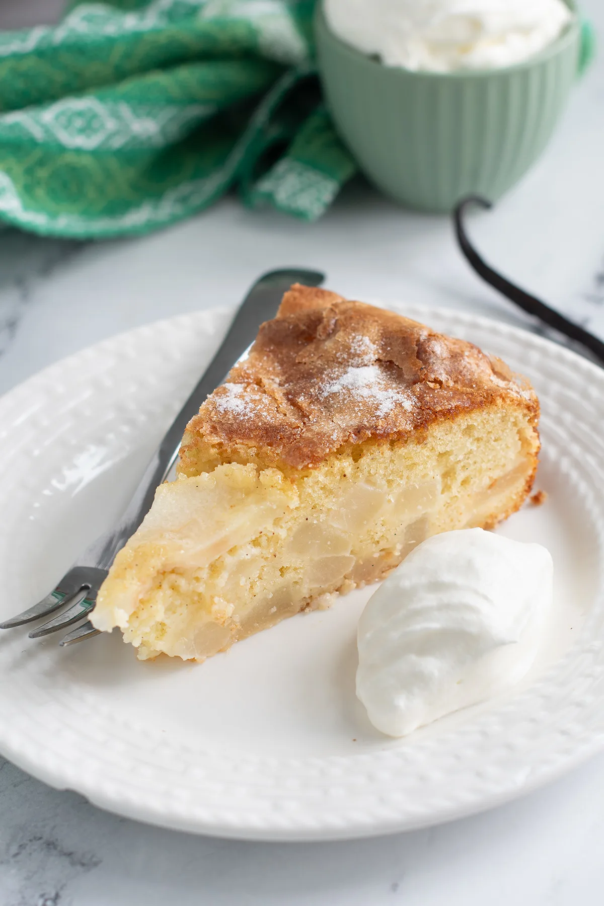 a slice of pear cake on a white plate with a fork and whipped cream.