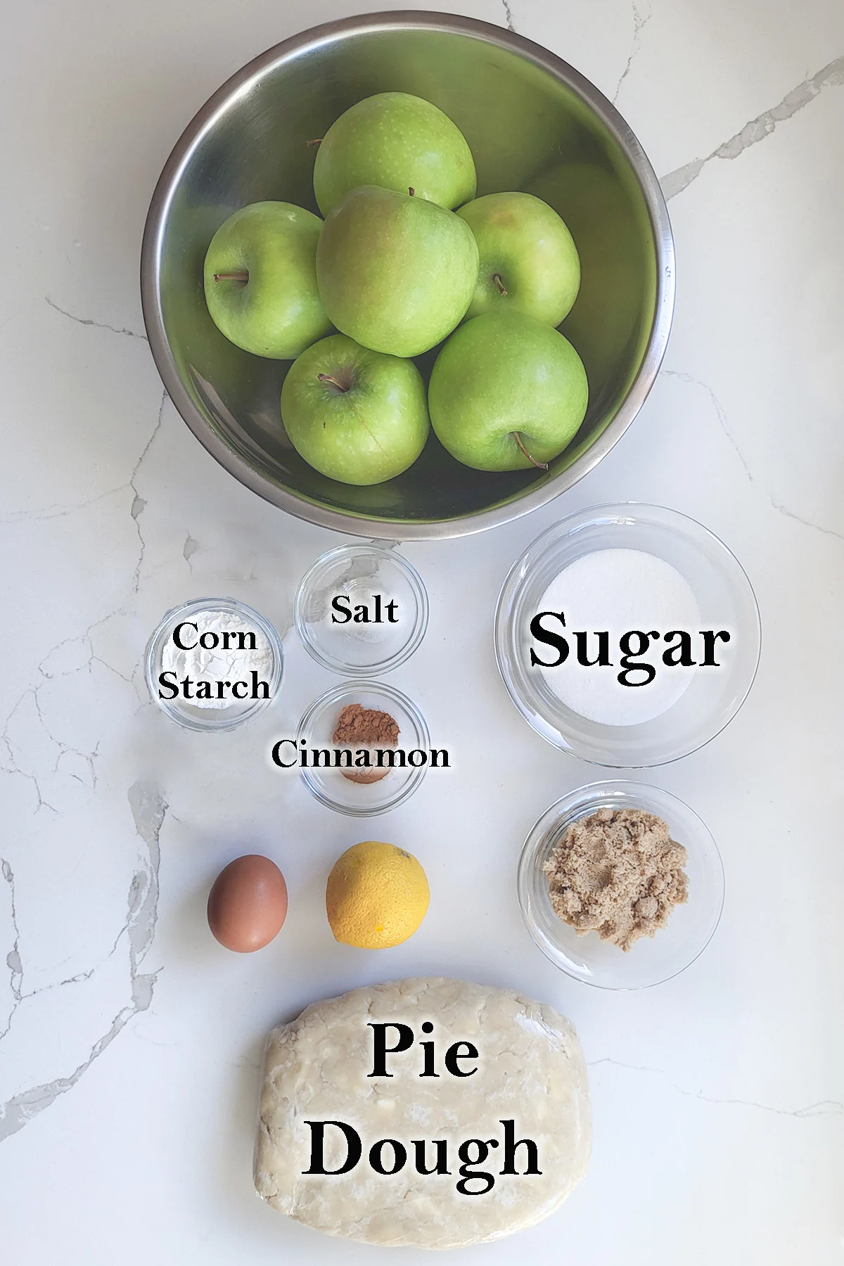 ingredients for apple pie in glass bowls on a white surface.