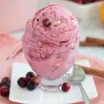 a glass bowl of cranberry ice cream on a white plate.