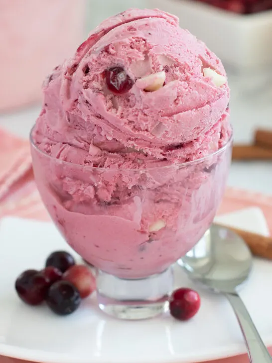a glass bowl of cranberry ice cream on a white plate.