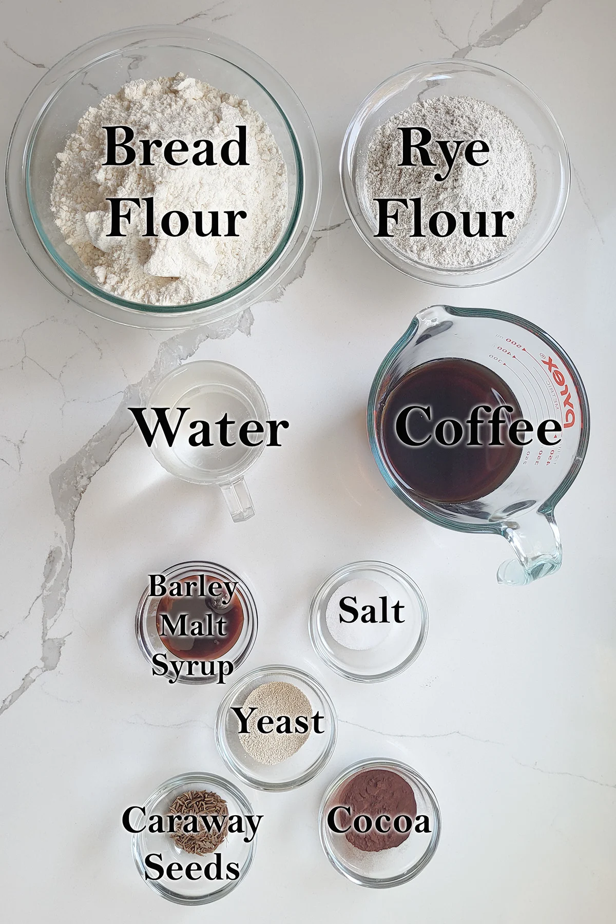 ingredients for marble rye bread in glass bowls on a white surface.