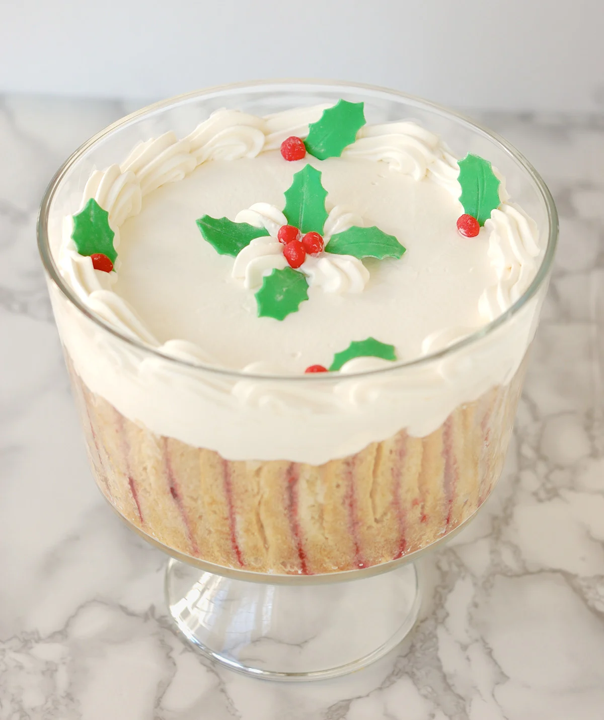 a glass bowl of trifle with holly decorations.