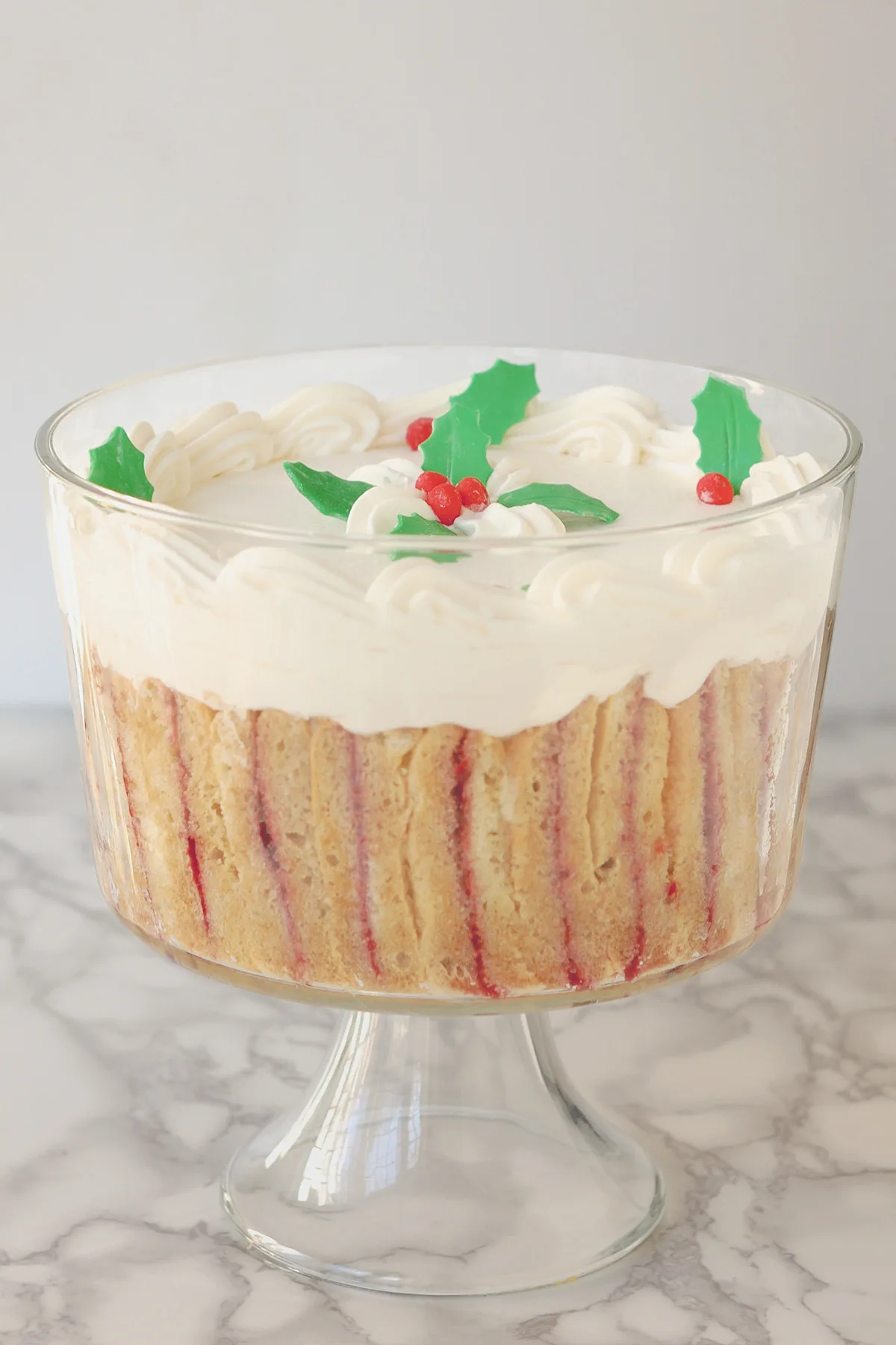 a glass bowl of trifle with holly decorations.