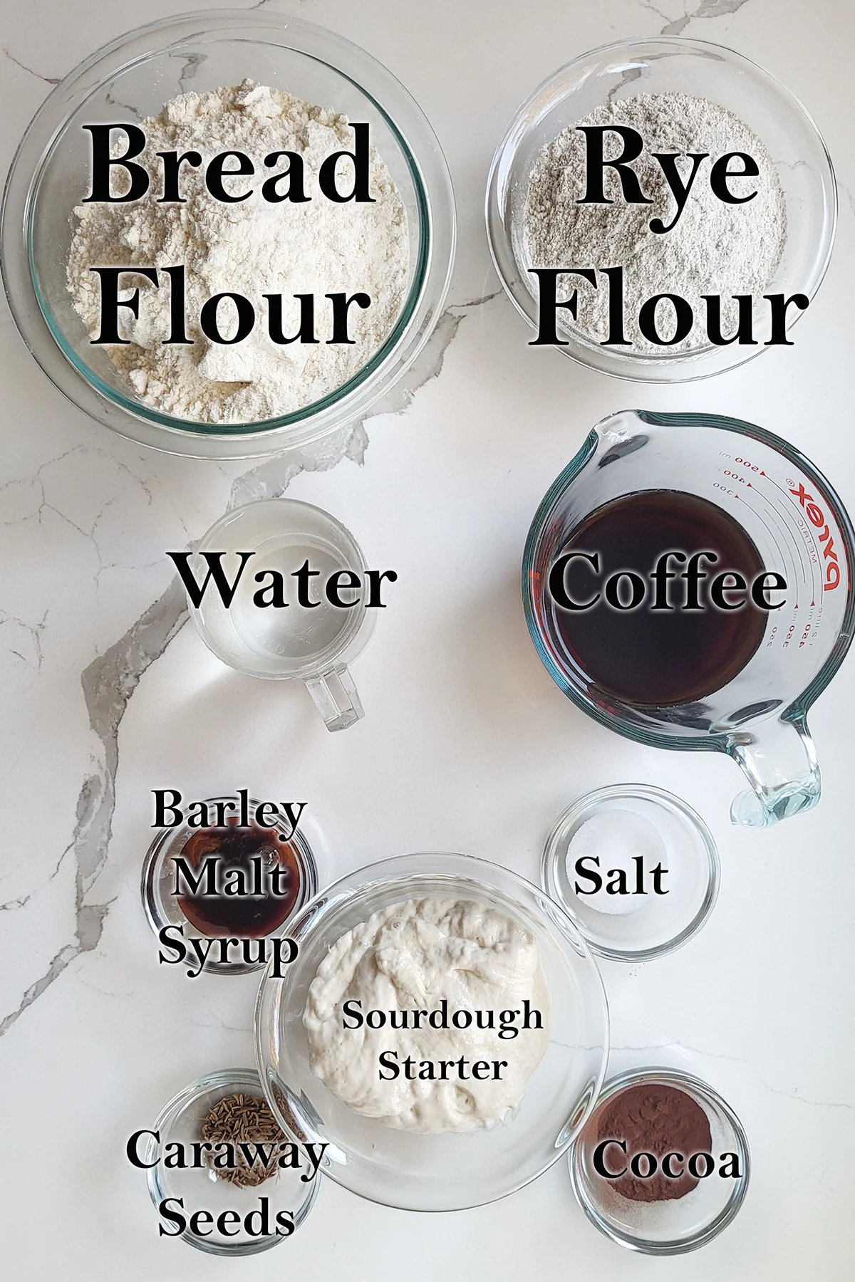 Ingredients for sourdough marble rye bread in glass bowls on a white surface.