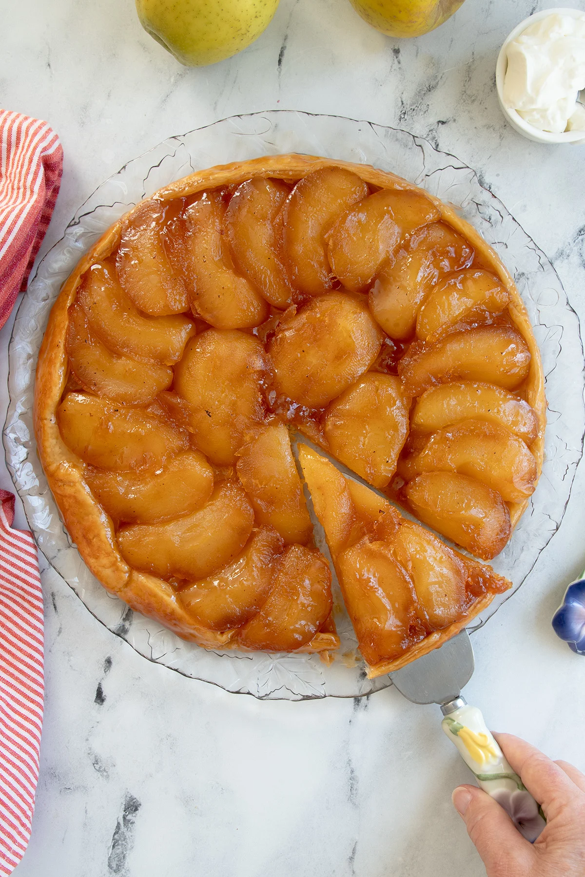 an apple tarte tatin on a glass serving plate with a wedge cut.