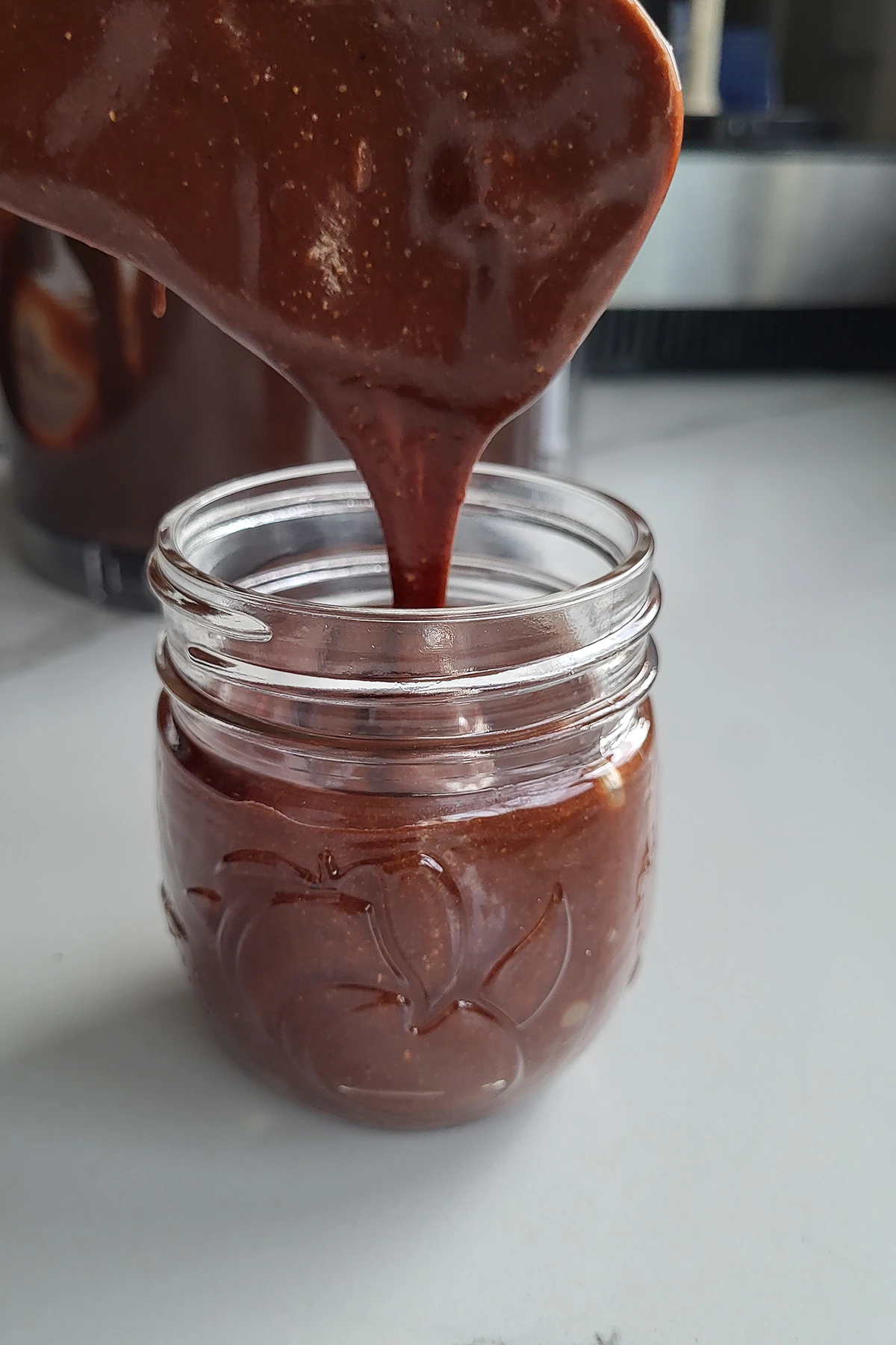 Chocolate spread pouring into a jar.