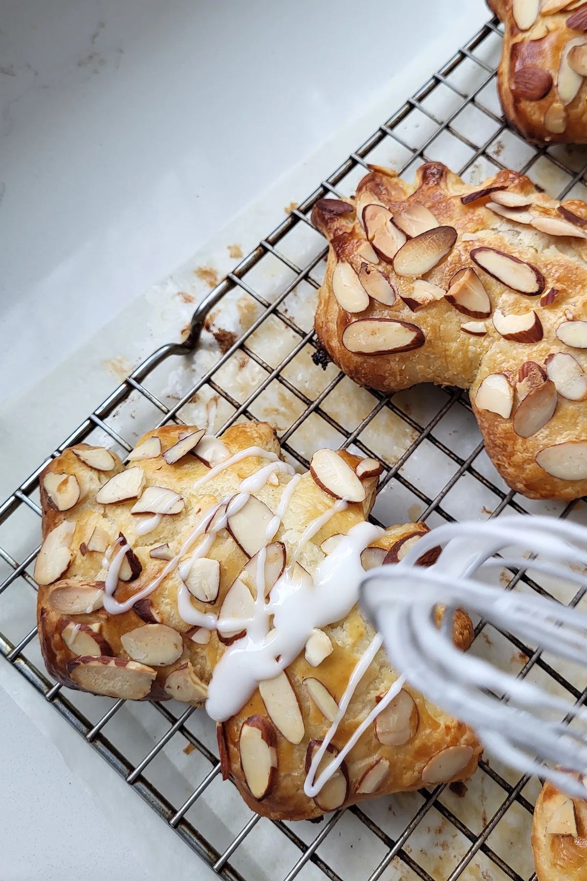 icing being drizzled on a bear claw pastry.