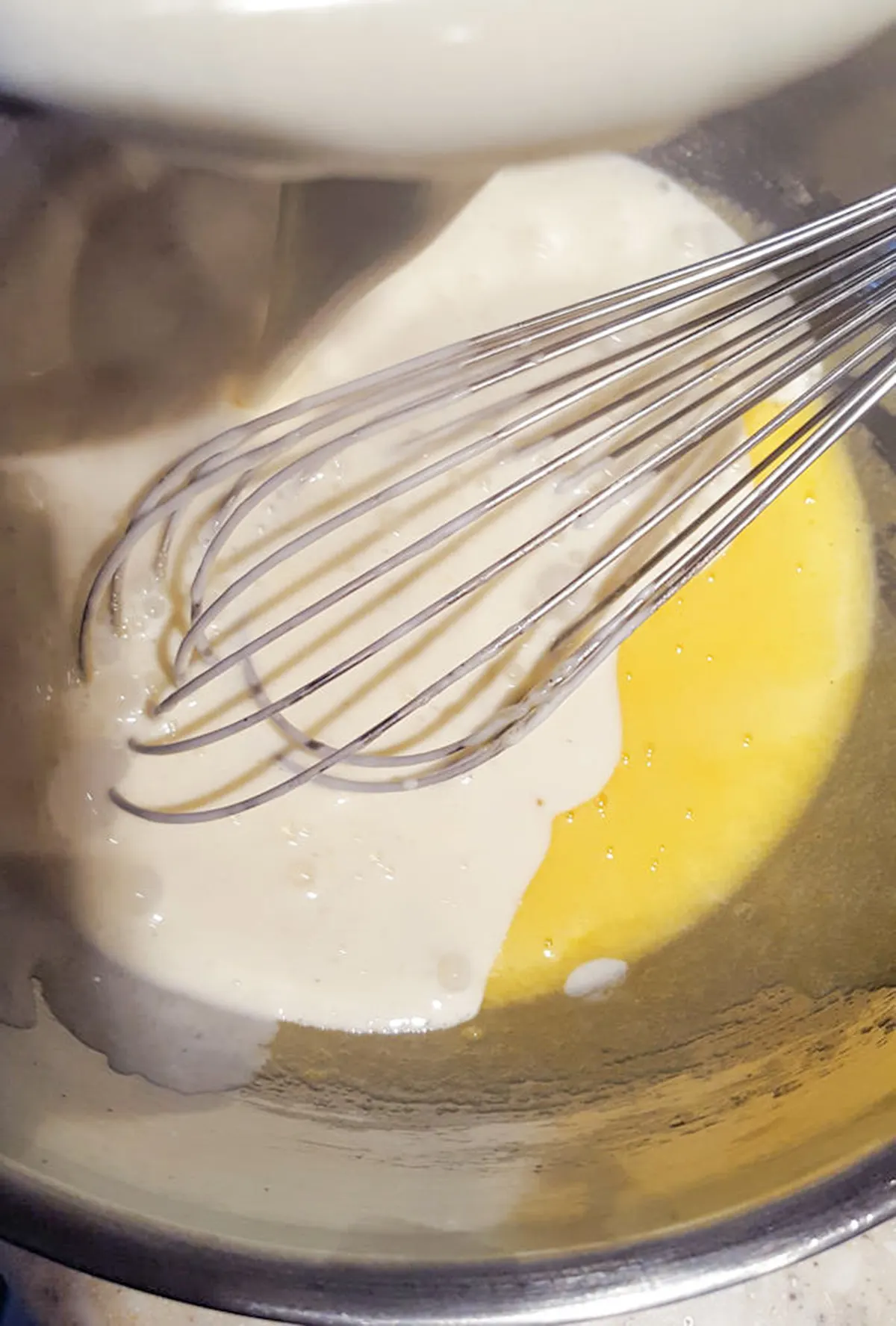 Egg yolks and hot cream in a bowl with a whisk.