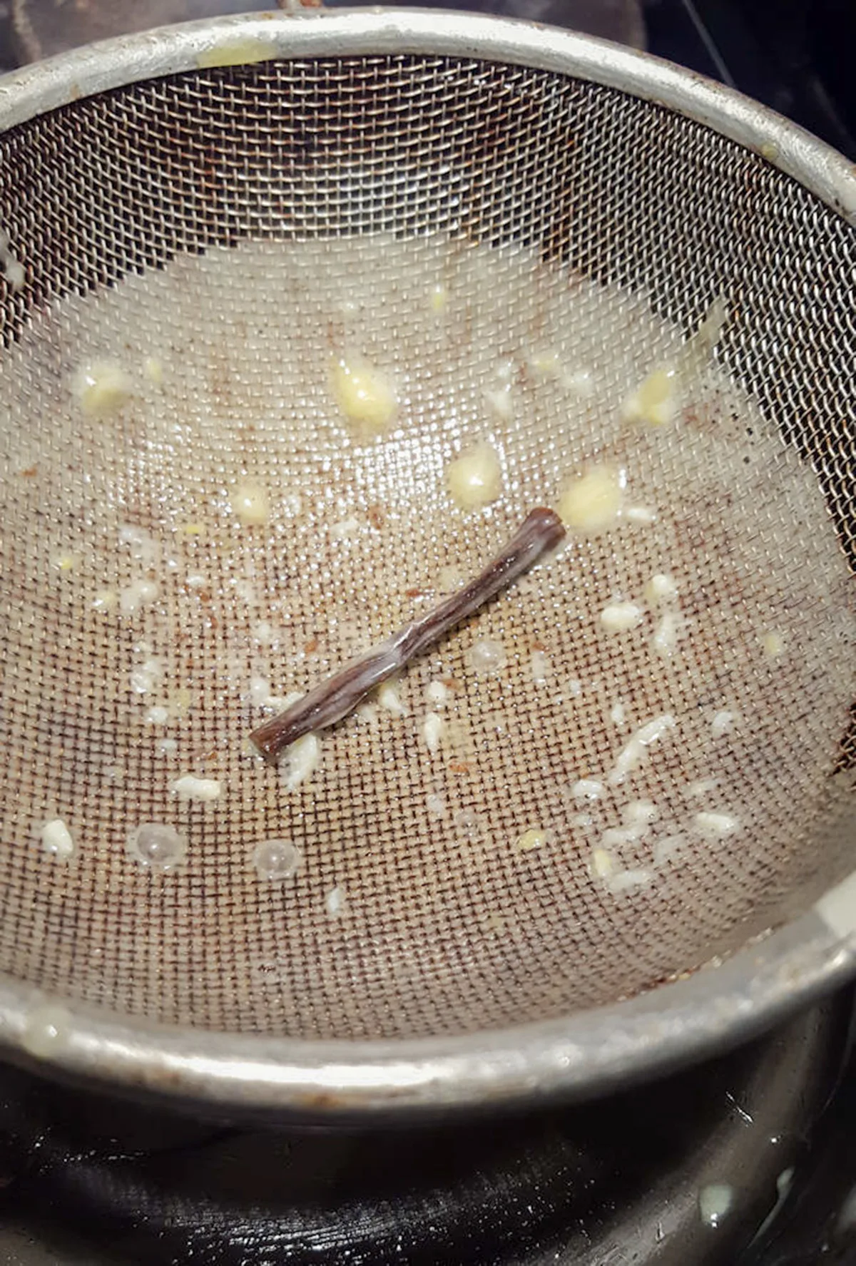 a strainer with bits of egg and a vanilla bean pod.