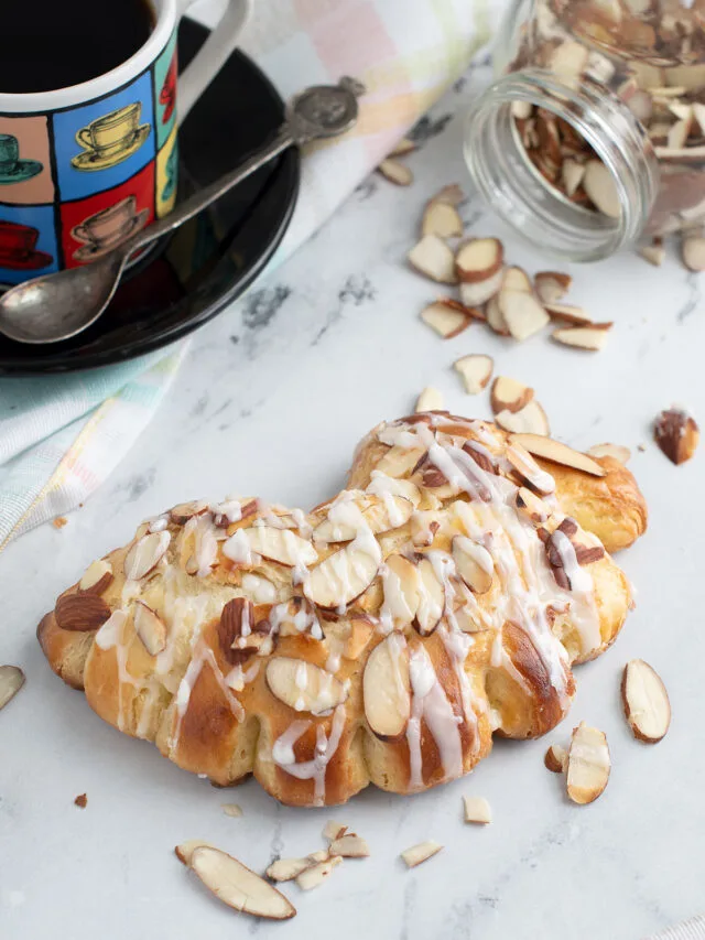 a bear claw pastry on a marble surface with a cup of coffee.