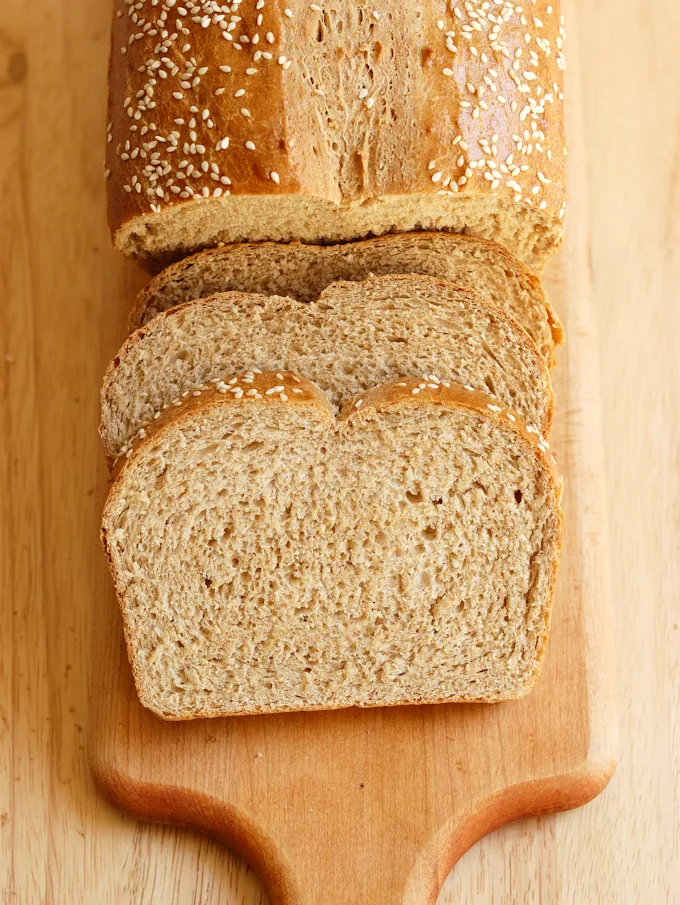  A sliced loaf of whole wheat bread on a cutting board.