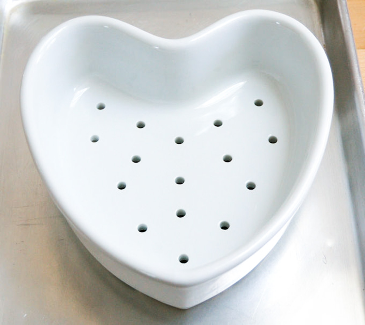 a heart shaped ceramic bowl with holes in the bottom.