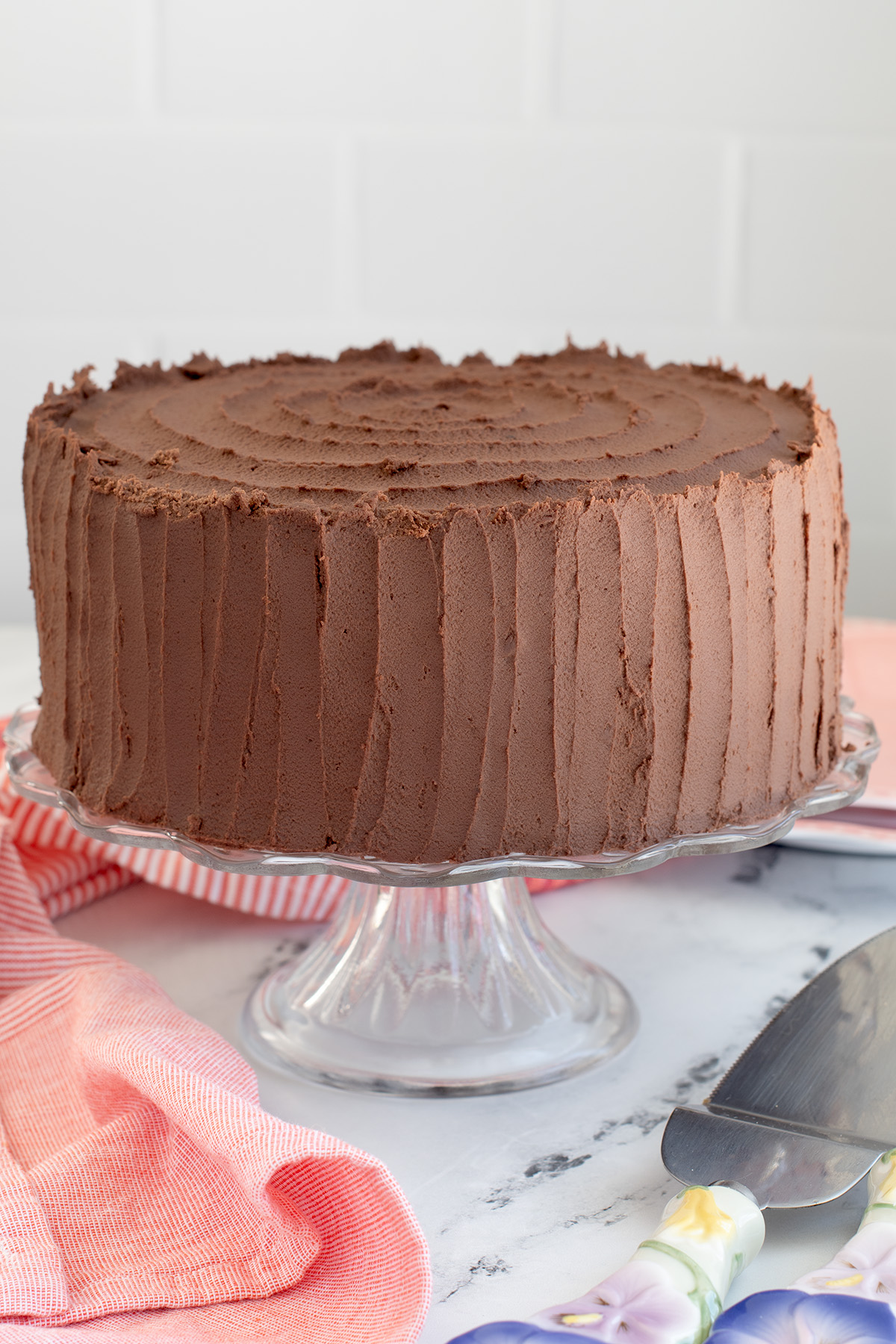 a chocolate iced cake on a glass cake stand.