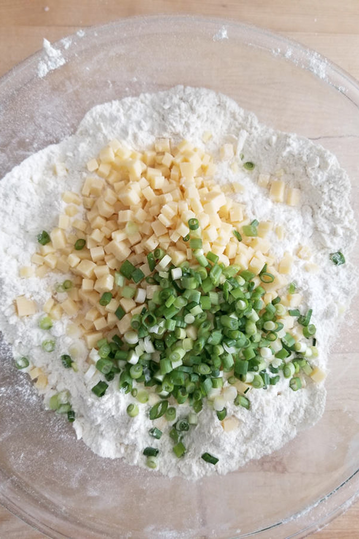 a bowl of flour with cubes of cheddar cheese and scallions on top.